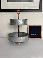 Front view of two-tier galvanized steel caddy with copper accents beside reference board