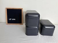 Three charcoal metal storage containers stacked beside felt board