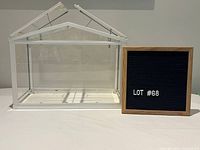 Front view of white metal and plexiglass greenhouse beside lot sign