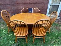 Oak pedestal dining table with six chairs displayed outdoors