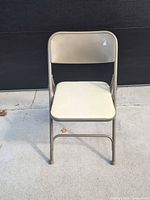 Front view of beige metal folding chair on concrete surface
