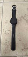 Front view of black Fitbit smartwatch with strap laid flat