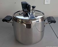 Front view of stainless steel pressure cooker showing lid, regulator, and handles