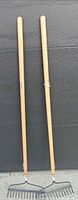 Full view of both wooden-handled garden rakes leaning upright