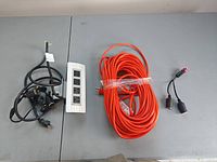 All items laid out: black multi-socket splitter, white 4-outlet power strip, orange extension cord, dual 12 V splitter