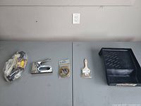 All five items laid out: bag of zip ties, metal staple gun, packaged bungee cord, packaged paintbrush, plastic paint tray