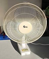 Front view of white Super table fan showing grille, center cap branding and control buttons