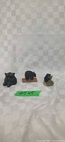 Three black bear figurines lined side by side on white backdrop