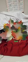Four painted metal maple leaves displayed on fabric backdrop