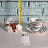 Horse paperweight, teacup and saucer grouped with ruler for scale