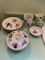 Group shot of all 12 Evesham pieces including stacked plates, casserole with lid, ramekins, small dish and cylindrical vase/utensil holder