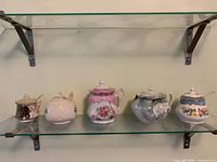 Five lidded porcelain jam or mustard pots on glass shelf