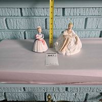 Both figurines side by side with tape measure for scale