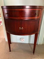 Front view of mahogany kidney-shaped cabinet showing drawer, tambour doors and brass hardware