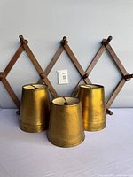 Front view of three standing and one lying gold lamp shades with wooden peg rack backdrop