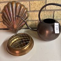 Copper shell mold, brass flower bowl with grid, and metal watering can group shot