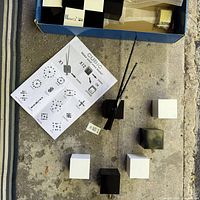 Clock kit components laid out: central mechanism, 12 cubes, instruction sheet, reeds possibly packaging