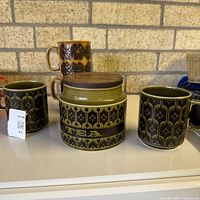 Hornsea tea caddy flanked by two Heirloom mugs and additional mug behind