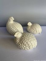Front view of three white ceramic quail figurines