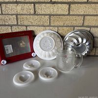 Group view of Etch A Sketch, plastic ring mold with maple leaf insert, aluminum bundt pan, three small motif inserts