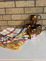 Overall lot view: stacked plaid napkins and four copper mugs