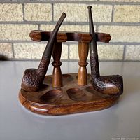 Two Brigham pipes resting on wooden stand