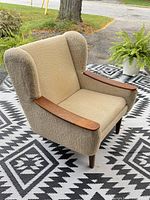 Front angled view of wingback chair showing teak arms, upholstery texture and tapered legs