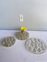 Three clear glass flower frogs displayed side by side, showing different diameters