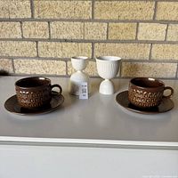 Group shot showing brown Pennine cup on saucer, second saucer, and two white Etruria egg cups