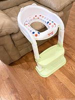 Potty seat assembled against couch showing front view, ladder and cushion visible