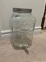 Full view of glass dispenser showing embossed brand, lid, spigot