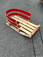 Full view of wooden sled with red rails and pull rope on asphalt surface