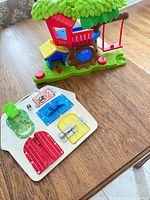 Plastic treehouse playset and wooden busy board on table