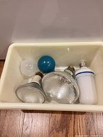 Five assorted light bulbs inside a plastic bin