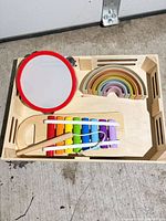 Overall view of tambourine, xylophone with mallet, and rainbow stacker in wooden tray