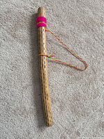 Full view of wooden rain stick showing perforations, pink wrap, and braided cord