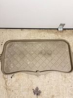 Top view of beige plastic shoe tray showing entire shape, lattice pattern and dirt