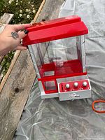 Overall view showing red and white tabletop claw machine with controls and clear panels