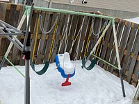 Full view of swing set showing frame, two belt swings, toddler swing, slide partially visible, snow covering