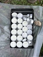Top view of box showing about 24 unused white tea lights in aluminum cups