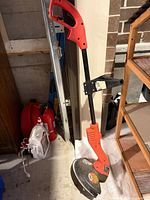 Full view of red and black corded string trimmer standing upright against wall