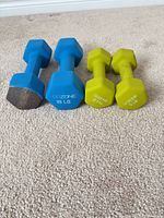 Two blue 10 lb and two lime green 5 lb GoZone hex dumbbells on carpet