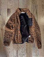 Front view of brown and black leopard print fleece jacket, unzipped to show interior pocket and lining