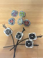 Five Beyblade tops and four ripcord launchers spread on wooden surface