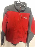 Front view showing red soft-shell body, dark grey shoulders/sleeves, zip pockets, chest logo