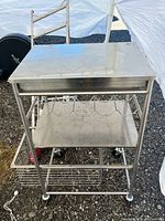 Front view of stainless steel kitchen cart showing top, drawer, wine rack shelf, basket shelf and casters
