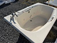 Full view of white Jacuzzi whirlpool bathtub showing jet nozzles, faucet, grab bars and drain
