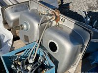 Underside view of two stainless steel sinks with attached hoses and crate of faucet parts