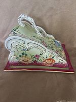 Right side view of domed porcelain cheese keeper showing floral pattern, scrolling relief and gold trim
