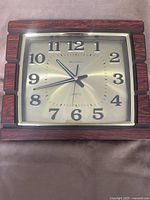 Front view showing brass-tone face, numerals, hands, and faux wood frame